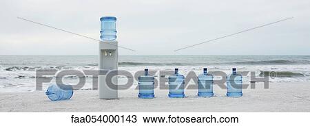 Stock Image - Water cooler and water jugs lined up on beach. Fotosearch