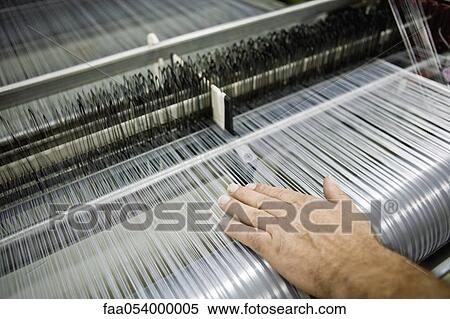 Stock Photography - Weaving mill, machinist manually checking thread tension on a loom. Fotosearch