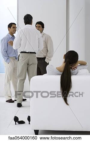 Woman relaxing in arm chair while male colleagues chat in background View Large Photo Image Stock Image - Woman relaxing in arm chair while male colleagues chat in background. Fotosearch
