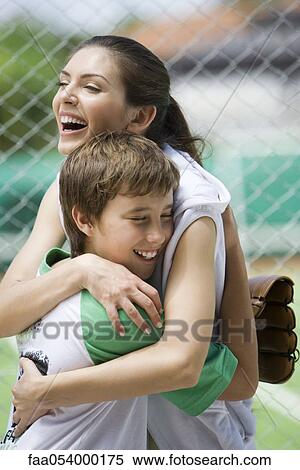 Stock Photography - Young baseball player embracing his mother. Fotosearch