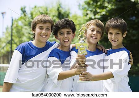 Stock Image - Young soccer teammates holding trophy together, portrait. Fotosearch