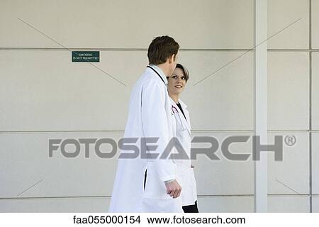 Doctors chatting and walking together along hospital corridor View Large Photo Image Picture - Doctors chatting and walking together along hospital corridor. Fotosearch