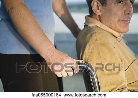 Man being pushed in wheelchair looking away contemplatively View Large Photo Image Picture - Man being pushed in wheelchair looking away contemplatively. Fotosearch