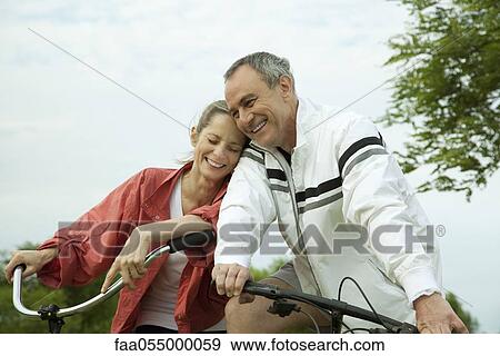 Stock Photo - Mature couple riding bikes, leaning against each other. Fotosearch