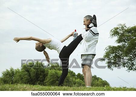Mature couple stretching in park, man holding woman's leg as she does backwards bend View Large Photo Image Picture - Mature couple stretching in park, man holding woman's leg as she does backwards bend. Fotosearch