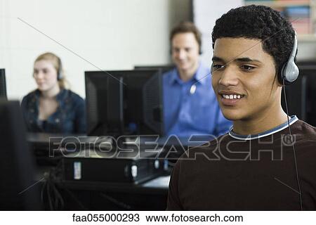Stock Image - Student listening to headphones in computer lab. Fotosearch