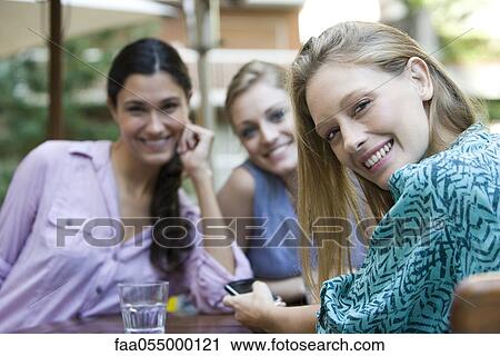 Stock Image - Young woman with friends at cafe. Fotosearch