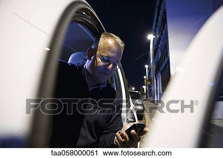 Man getting out of car, looking at cell phone View Large Photo Image Stock Image - Man getting out of car, looking at cell phone. Fotosearch