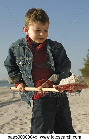 Stock Photography - Boy digging with shovel on sandy beach. Fotosearch