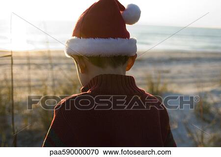 Boy exploring outdoors wearing Santa hat, beach in background View Large Photo Image Stock Image - Boy exploring outdoors wearing Santa hat, beach in background. Fotosearch