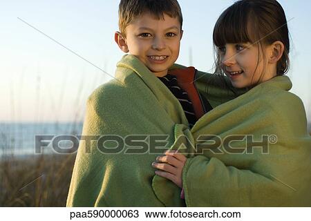 Stock Image - Children wrapped together in blanket outdoors, portrait. Fotosearch