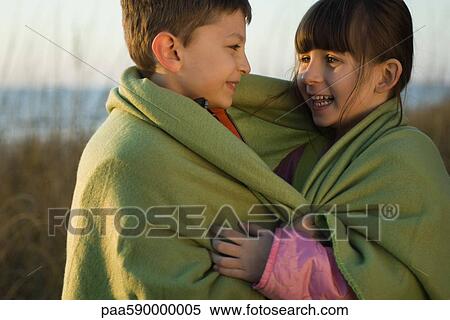 Stock Photography - Children wrapped together in blanket outdoors, portrait. Fotosearch