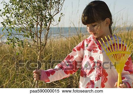 Girl with gardening rake touching trunk of sapling View Large Photo Image Stock Photography - Girl with gardening rake touching trunk of sapling. Fotosearch