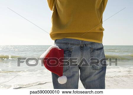 Man standing on beach looking at view, Santa hat in back pocket View Large Photo Image Stock Image - Man standing on beach looking at view, Santa hat in back pocket. Fotosearch