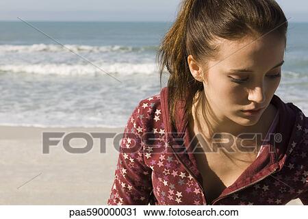 Stock Image - Preteen girl at beach contemplatively looking down. Fotosearch