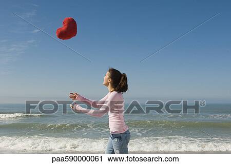 Preteen girl at beach tossing stuffed heart-shaped toy into air View Large Photo Image Stock Image - Preteen girl at beach tossing stuffed heart-shaped toy into air. Fotosearch