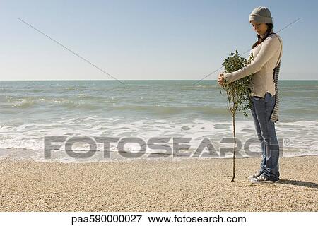 Stock Photo - Preteen girl hugging tree growing at water's edge on beach. Fotosearch