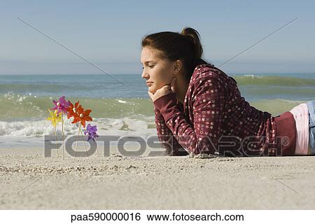 Preteen girl lying on stomach on beach, contemplatively looking at pinwheels stuck in the sand View Large Photo Image Stock Photograph - Preteen girl lying on stomach on beach, contemplatively looking at pinwheels stuck in the sand. Fotosearch