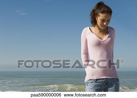 Stock Photograph - Preteen girl on beach contemplatively looking down. Fotosearch
