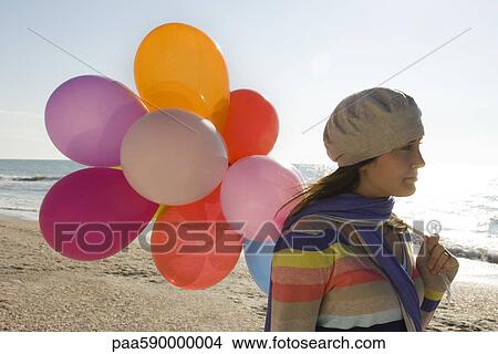 Picture - Preteen girl with bunch of balloons walking on beach. Fotosearch