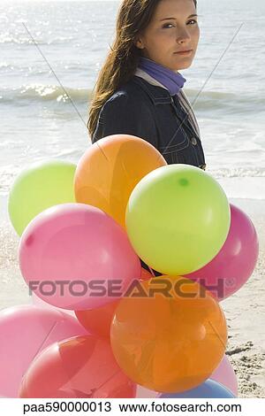 Stock Image - Preteen girl with bunch of balloons walking on beach. Fotosearch