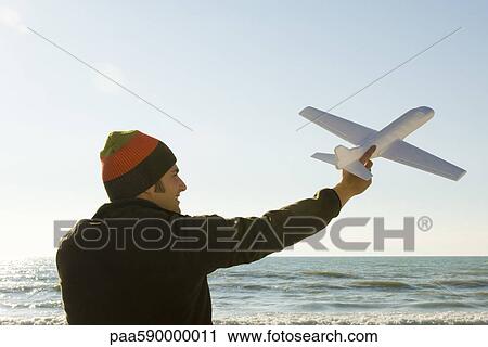 Young man at beach holding aloft toy airplane View Large Photo Image Stock Image - Young man at beach holding aloft toy airplane. Fotosearch