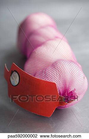 Stock Image - Mesh bag containing four garlic bulbs. Fotosearch