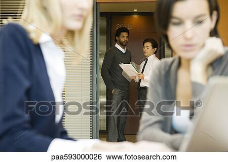 Stock Photograph - Executives discussing document in office doorway. Fotosearch