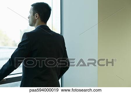 Young businessman looking out window in thought View Large Photo Image Stock Photo - Young businessman looking out window in thought. Fotosearch