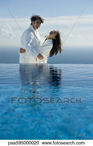 Couple embracing and laughing at edge of infinity pool, both wearing bathrobes View Large Photo Image Stock Image - Couple embracing and laughing at edge of infinity pool, both wearing bathrobes. Fotosearch
