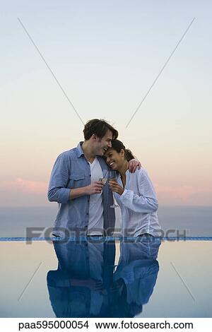 Couple embracing at edge of infinity pool, enjoying champagne View Large Photo Image Picture - Couple embracing at edge of infinity pool, enjoying champagne. Fotosearch
