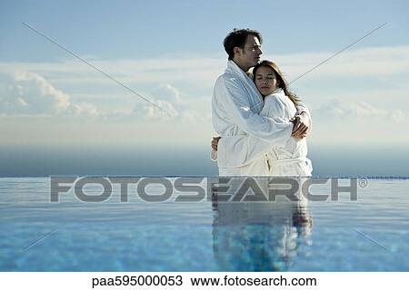 Couple embracing at edge of infinity pool, both wearing bathrobes View Large Photo Image Stock Image - Couple embracing at edge of infinity pool, both wearing bathrobes. Fotosearch