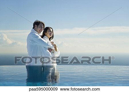 Stock Photo - Couple embracing at edge of infinity pool, both wearing bathrobes. Fotosearch