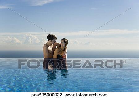 Stock Image - Couple relaxing together next to infinity pool. Fotosearch