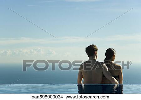 Couple standing at edge of infinity pool, looking at view View Large Photo Image Picture - Couple standing at edge of infinity pool, looking at view. Fotosearch