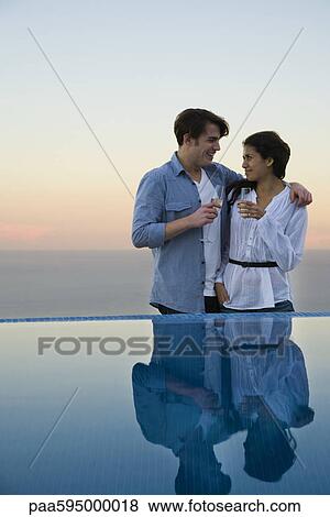 Stock Photo - Couple standing at edge of infinity pool, enjoying champagne. Fotosearch