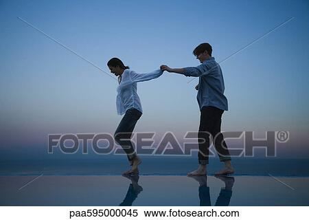 Stock Photography - Couple walking together along edge of infinity pool, holding hands. Fotosearch