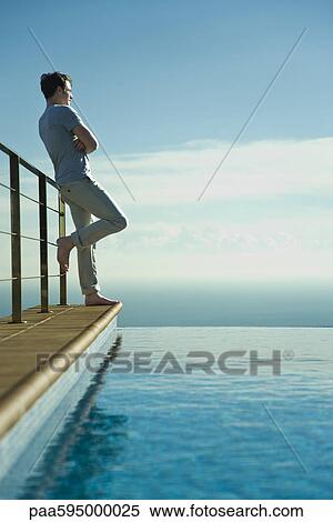 Man leaning against railing beside infinity pool, looking at view View Large Photo Image Stock Photography - Man leaning against railing beside infinity pool, looking at view. Fotosearch