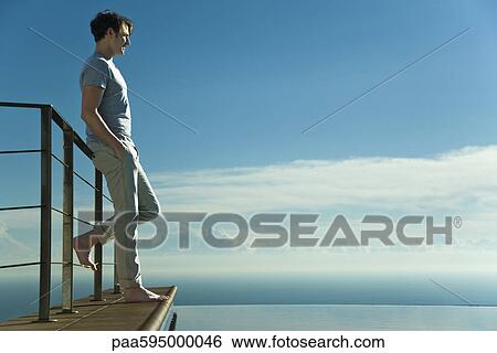 Stock Photograph - Man leaning against railing, looking at view. Fotosearch