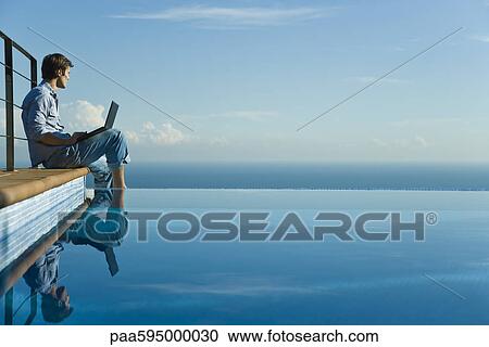 Man sitting at edge of infinity pool with laptop computer, looking at view View Large Photo Image Stock Image - Man sitting at edge of infinity pool with laptop computer, looking at view. Fotosearch