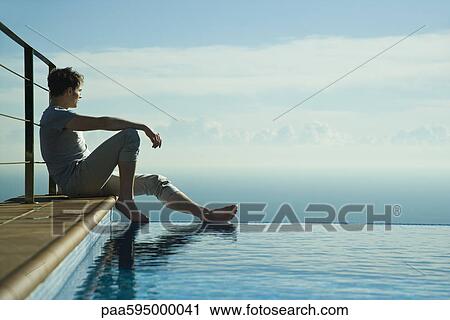 Man sitting on edge of infinity pool, looking at view View Large Photo Image Stock Image - Man sitting on edge of infinity pool, looking at view. Fotosearch