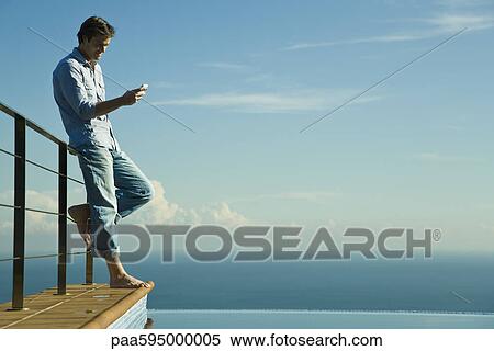 Man standing beside infinity pool, text messaging with cell phone View Large Photo Image Stock Photography - Man standing beside infinity pool, text messaging with cell phone. Fotosearch