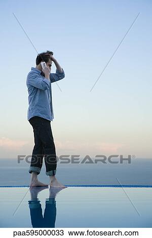 Man walking on edge of infinity pool, talking on cell phone View Large Photo Image Stock Image - Man walking on edge of infinity pool, talking on cell phone. Fotosearch