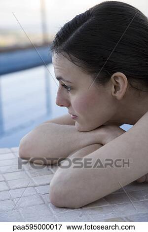 Stock Photo - Woman lying beside pool with head resting on arms, cropped. Fotosearch