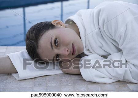 Stock Image - Woman lying on side next to pool, portrait. Fotosearch