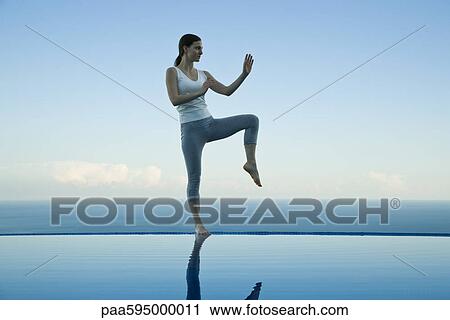 Stock Image - Woman practicing Tai Chi Chuan on edge of infinity pool. Fotosearch