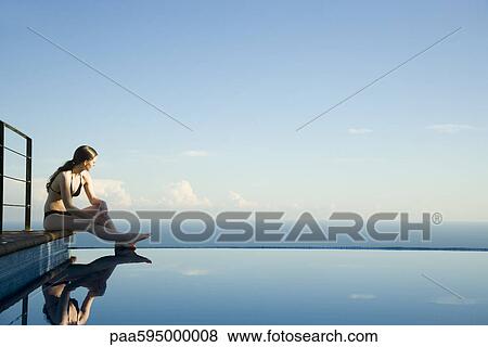 Woman sitting at edge of infinity pool, looking at view View Large Photo Image Stock Photo - Woman sitting at edge of infinity pool, looking at view. Fotosearch