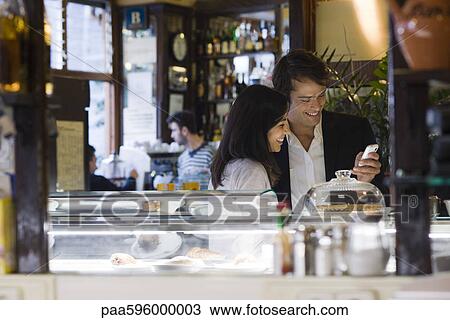 Stock Image - Couple looking at cell phone together in cafe. Fotosearch