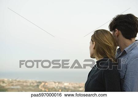 Couple embracing, looking at view View Large Photo Image Stock Photograph - Couple embracing, looking at view. Fotosearch