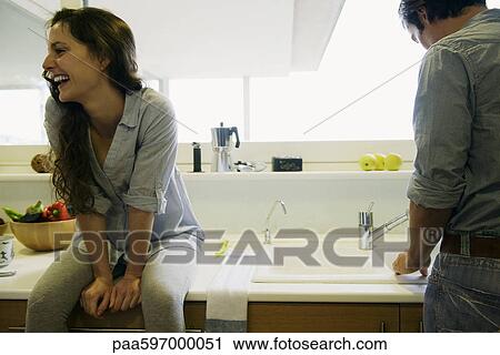 Couple in kitchen, man washing dishes, woman sitting on counter laughing View Large Photo Image Stock Image - Couple in kitchen, man washing dishes, woman sitting on counter laughing. Fotosearch